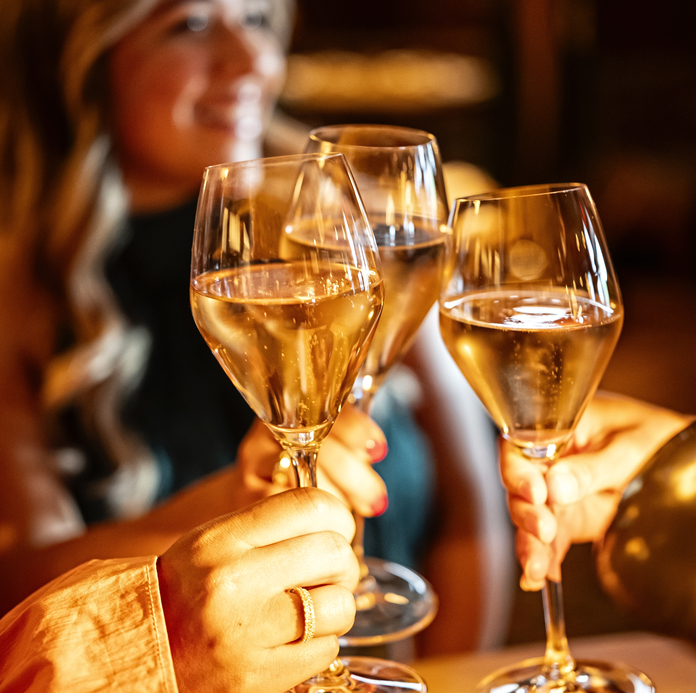 Three hands holding wine glasses in a celebratory toast, with a blurred woman in the background.