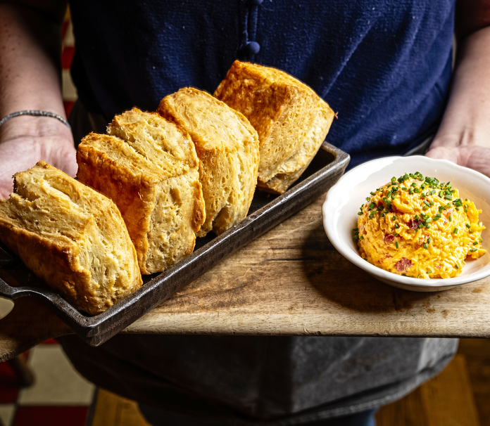 Person holding tray with golden-brown biscuits and bowl of creamy mac and cheese.