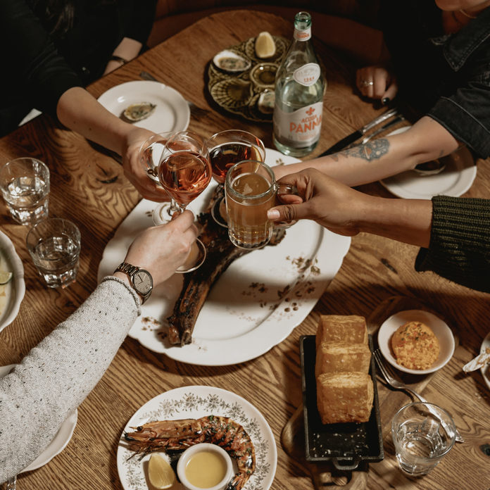 Group toasting with drinks and plates of food including shrimp, bread, and oysters on a wooden table.