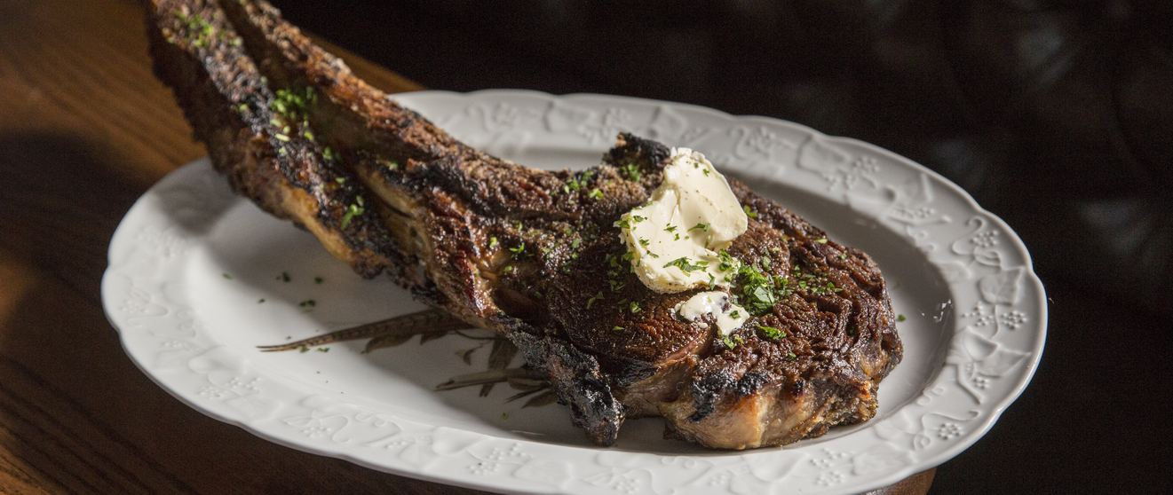 Grilled ribeye steak with herbs and butter served on a white plate.