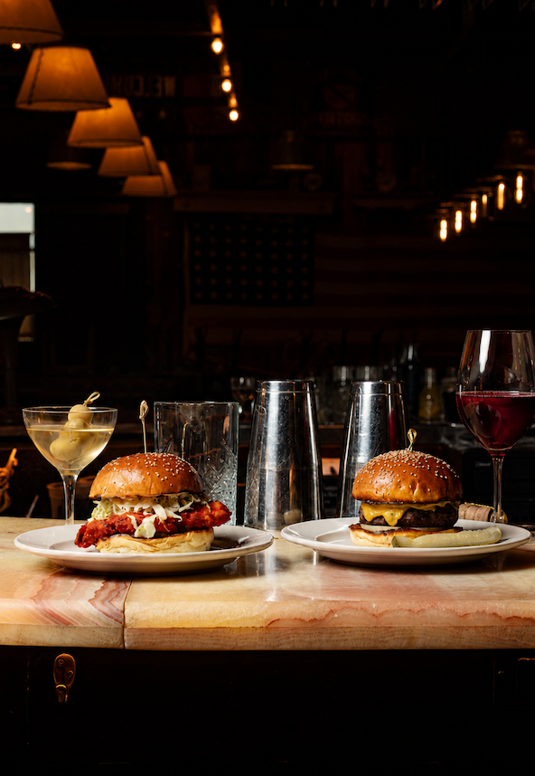 A fried chicken sandwich and smash burger served with a dirty martini and glass of red wine at Anselm's dimly lit bar