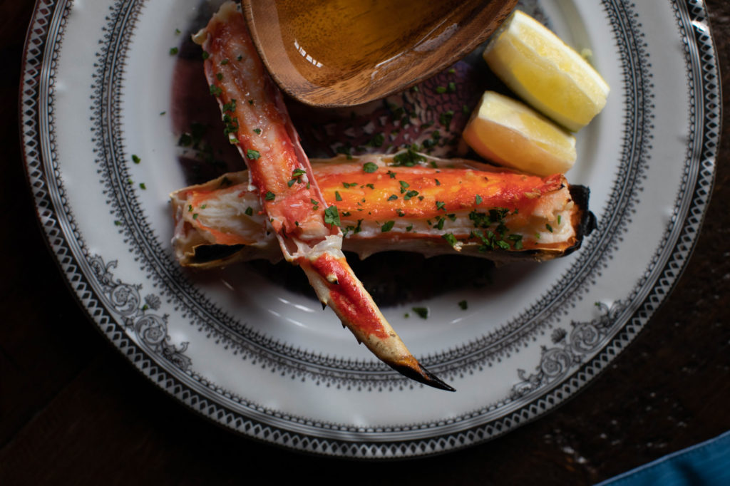 Tableview from above of King crab leg served with drawn butter and lemon wedges.