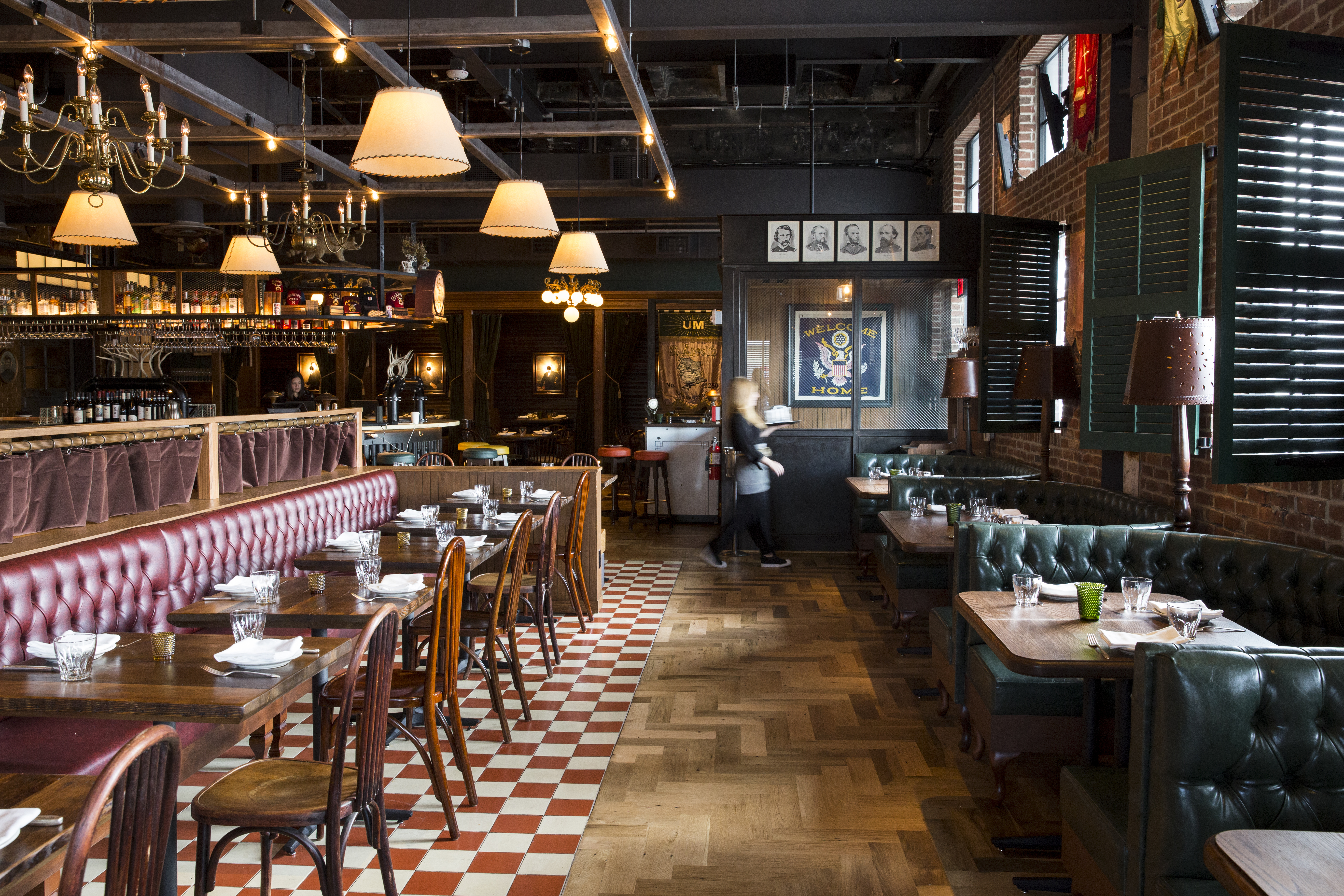 Dining room with parquet floors and checkered floors decorated with vintage light fixtures and tufted dark green booths.
